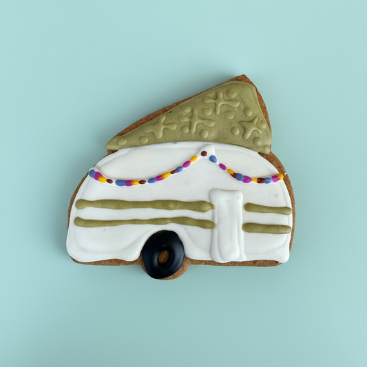 Decorative cookie shaped like a camper with lights and a Christmas tree on top