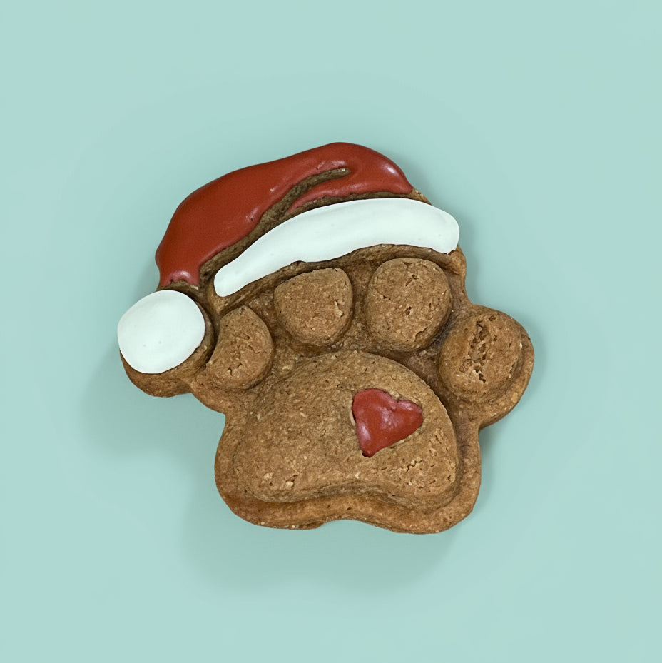 Dog treat shaped like a paw with a Santa hat and red heart on a light blue background