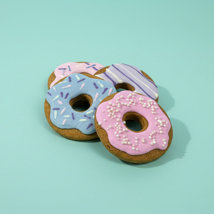 Three donut-shaped cookies with colorful icing and sprinkles on a wooden surface